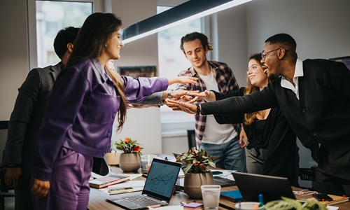 A team of diverse coworkers celebrate a successful project in their office with enthusiasm and teamwork, showing collaboration and achievement.