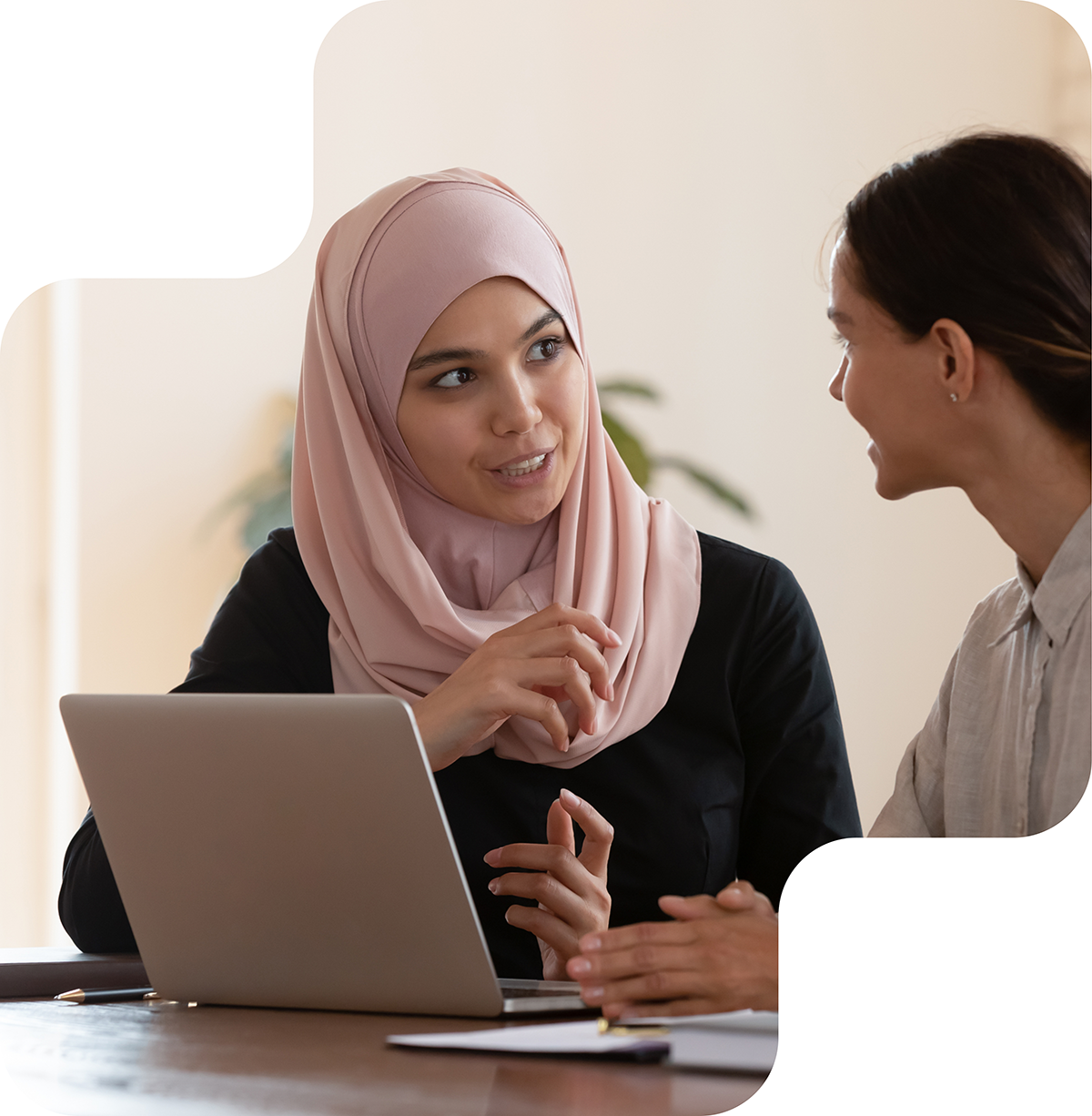 Two colleagues engaged in a thoughtful conversation, with one woman wearing a hijab, showcasing diversity and meaningful dialogue in the workplace.