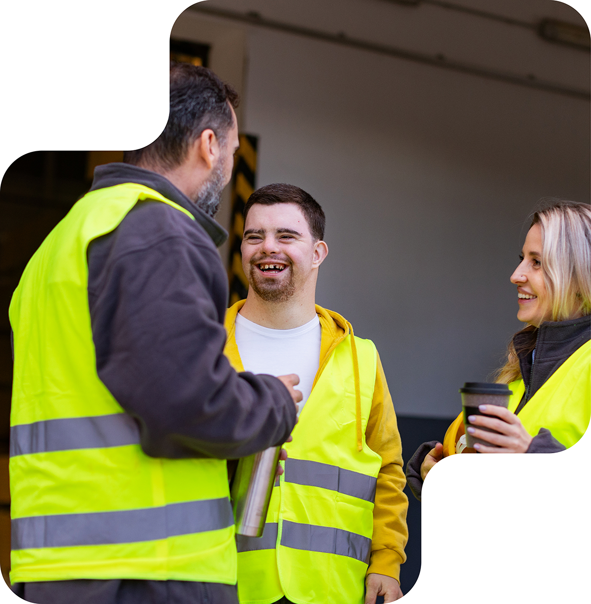 Image shows two men, one of whom has Down syndrome, engaged in a cheerful conversation. Both are wearing reflective vests. The man with Down syndrome is smiling broadly, displaying a sense of happiness. The background features a contrasting orange and beige color scheme. The interaction between the two men appears friendly and positive.