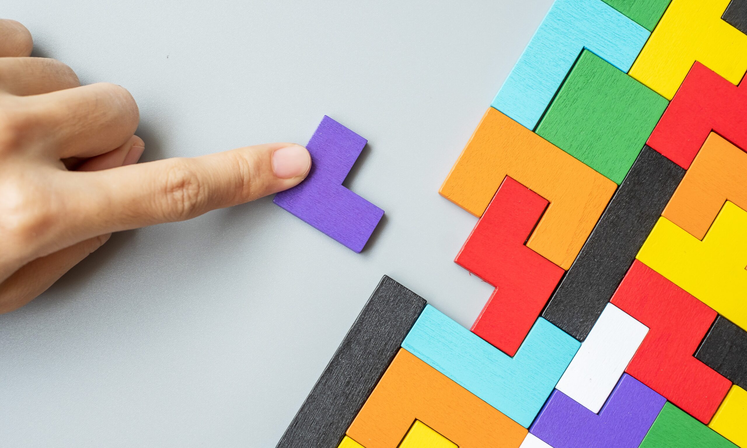 Hand placing a purple puzzle piece into a colorful puzzle, symbolizing inclusive decision-making and teamwork.