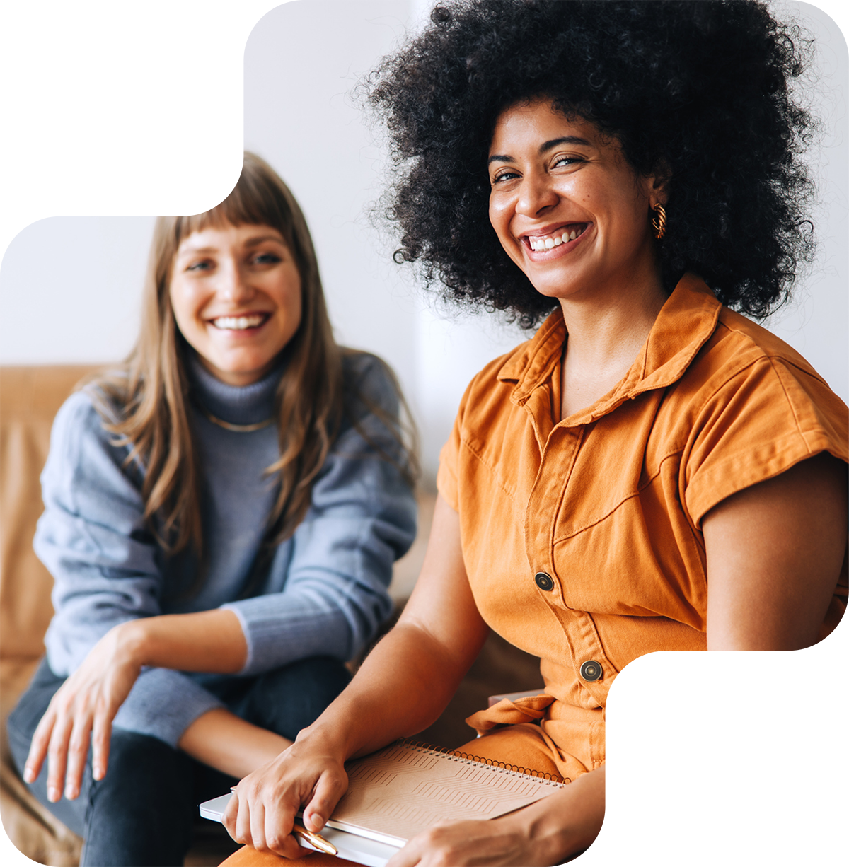 Black young woman in the workplace sitting next to a white woman smiling as friends and peers