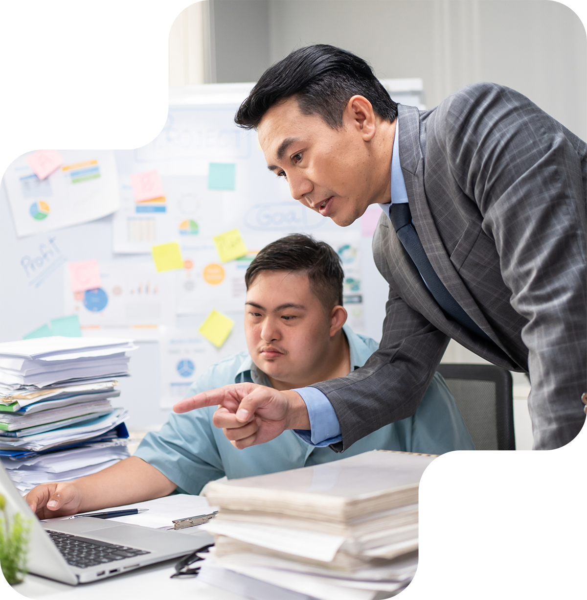 Business man pointing to a computer screen in helpful manner, standing next to a neurodiverse employee