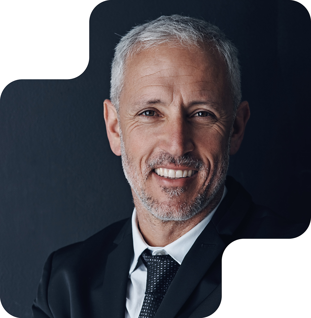 Image shows an older man with short, gray hair and a neatly trimmed beard, smiling warmly at the camera. He is wearing a suit and tie. The image conveys a sense of confidence, approachability, and professionalism.