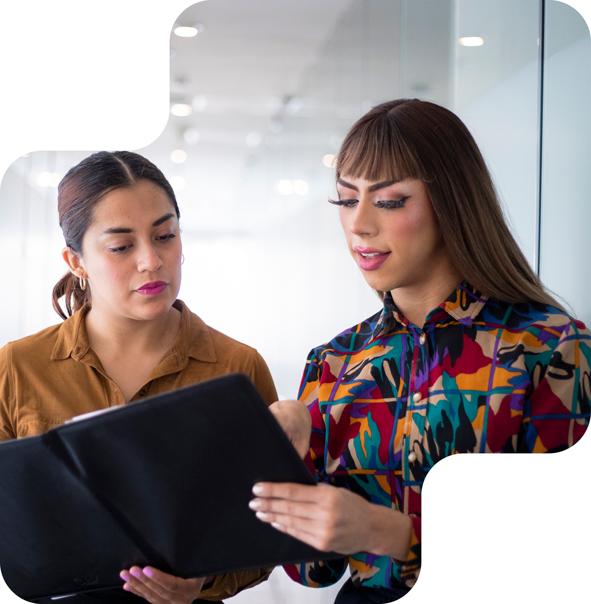 Transgender woman standing next to a Latina woman looking at a folder of notes together