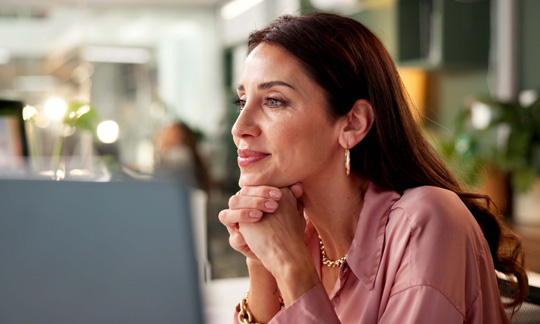 Professional woman thoughtfully looking at a laptop screen in a modern office setting
