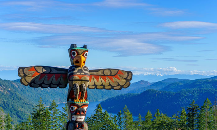 Totem pole overlooking a mountainous forest landscape in the Pacific Northwest, representing Indigenous art and connection to land